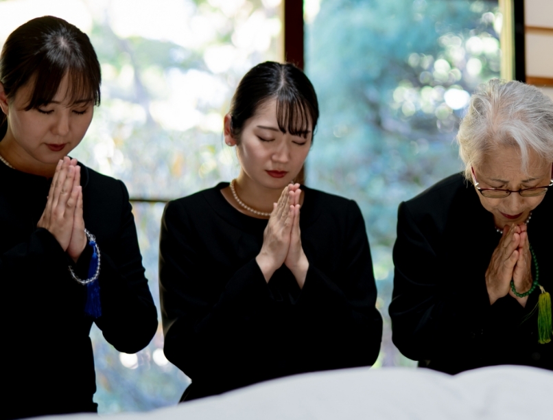 室内で故人に手を合わせる喪服を着た女性3人
